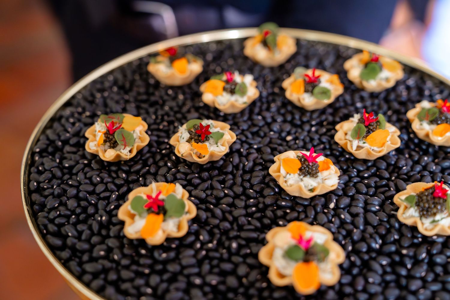 Elegant appetizer tray with phyllo cups filled with colorful toppings, displayed on black beans at a catered event.