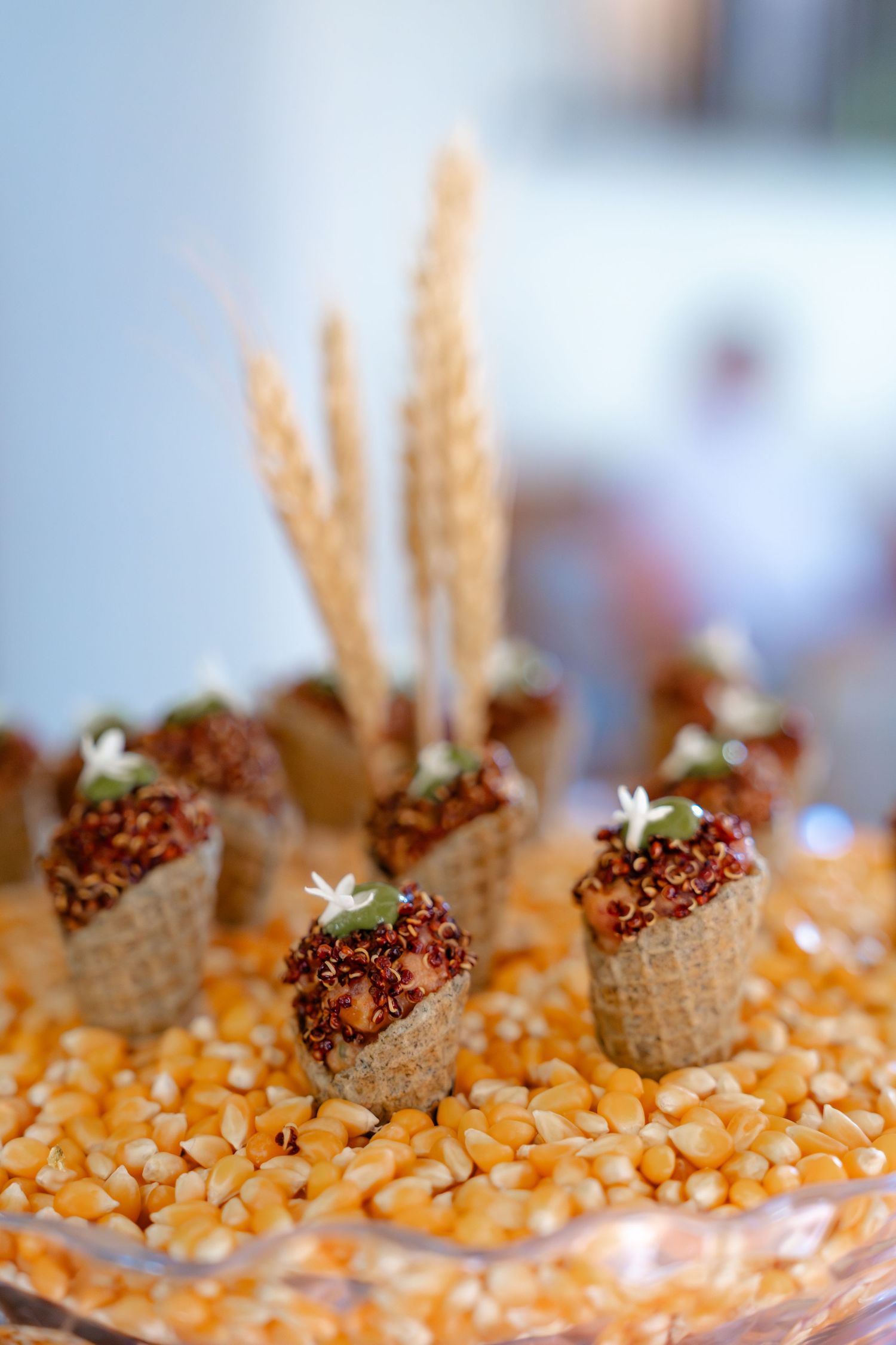 Elegant appetizers in waffle cones filled with quinoa, displayed on corn kernels with wheat stalks decoration.