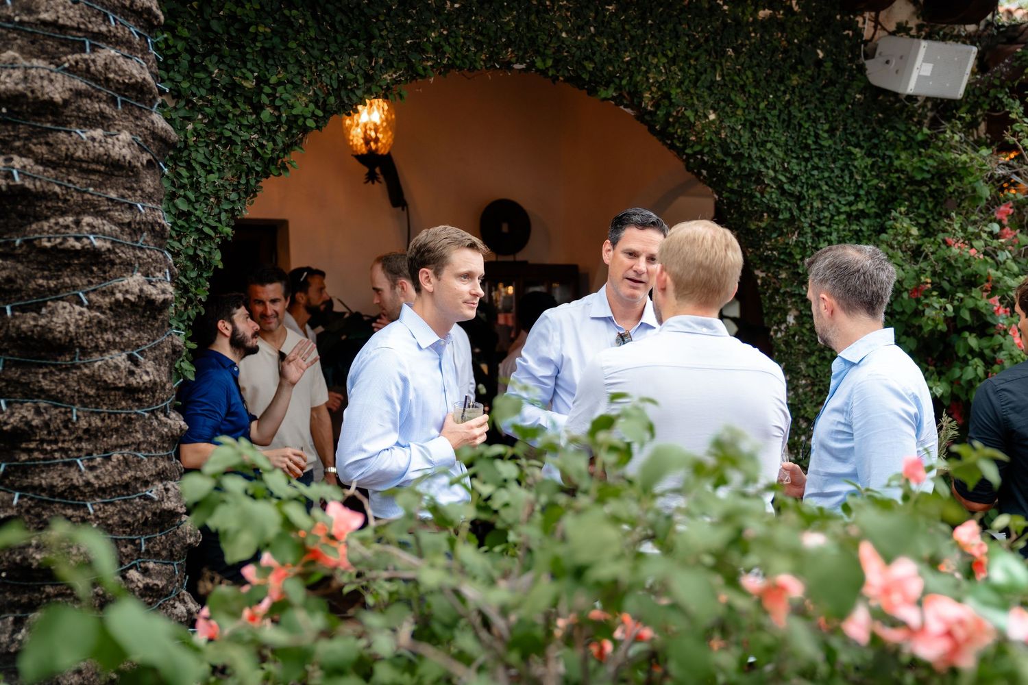 Men in light blue shirts networking at an elegant outdoor garden party venue.