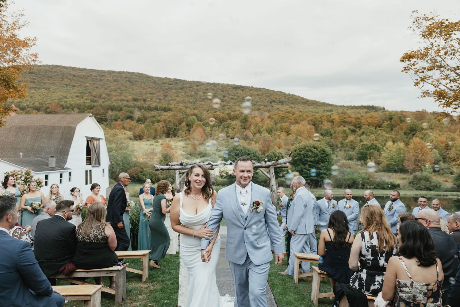 Wedding ceremony setup with white chairs on a lush green lawn facing a historic stone church under cloudy skies.