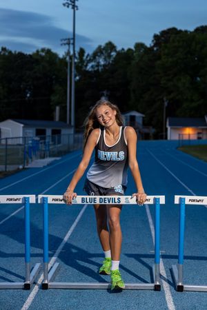 Female track athlete in Blue Devils uniform posing at hurdles.