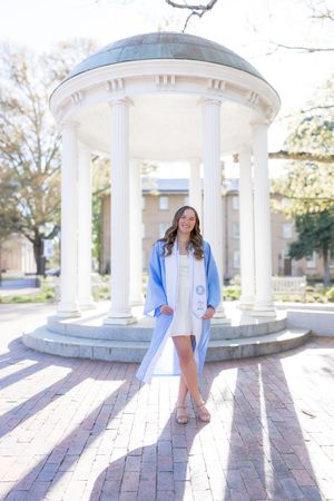 Young woman in light blue graduation gown and stole posing at the Old Well at UNC Chapel Hill.