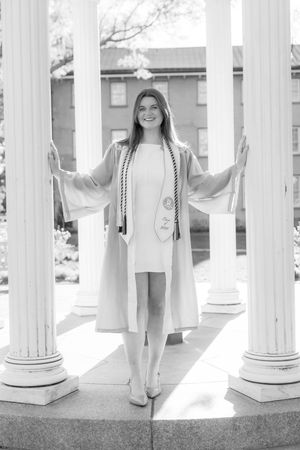 Graduate in cap and gown posing between white columns at UNC Chapel Hill in black and white photo.
