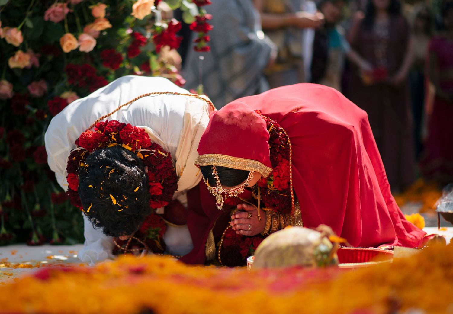 Bride and groom bowing during a traditional Indian wedding ceremony surrounded by vibrant floral decorations.