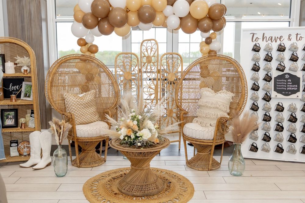Boho bridal shower setup with rattan peacock chairs, balloon arch, floral centerpiece, and photo booth backdrop.