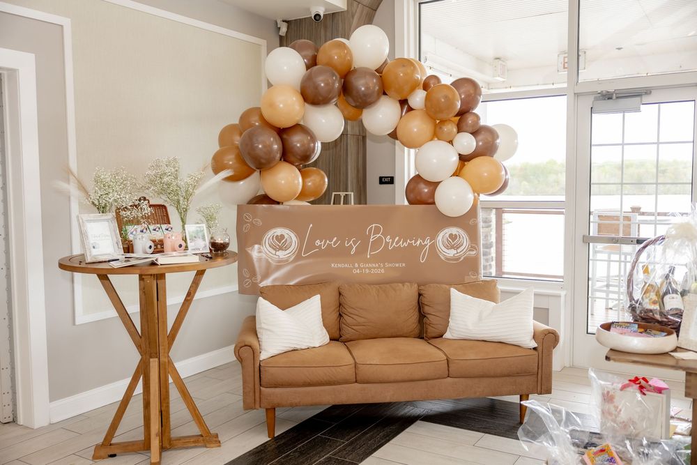 Brown leather sofa with balloon arch garland and Love is Brewing banner for a bridal shower party.