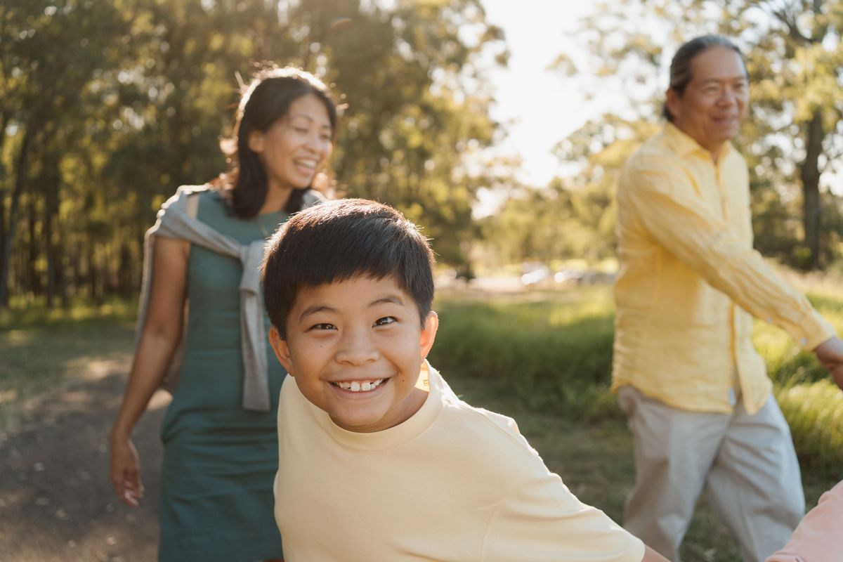 Smiling boy with parents walking in a sunny park, enjoying a happy family outdoor adventure together during a family photoshoot in sydney
