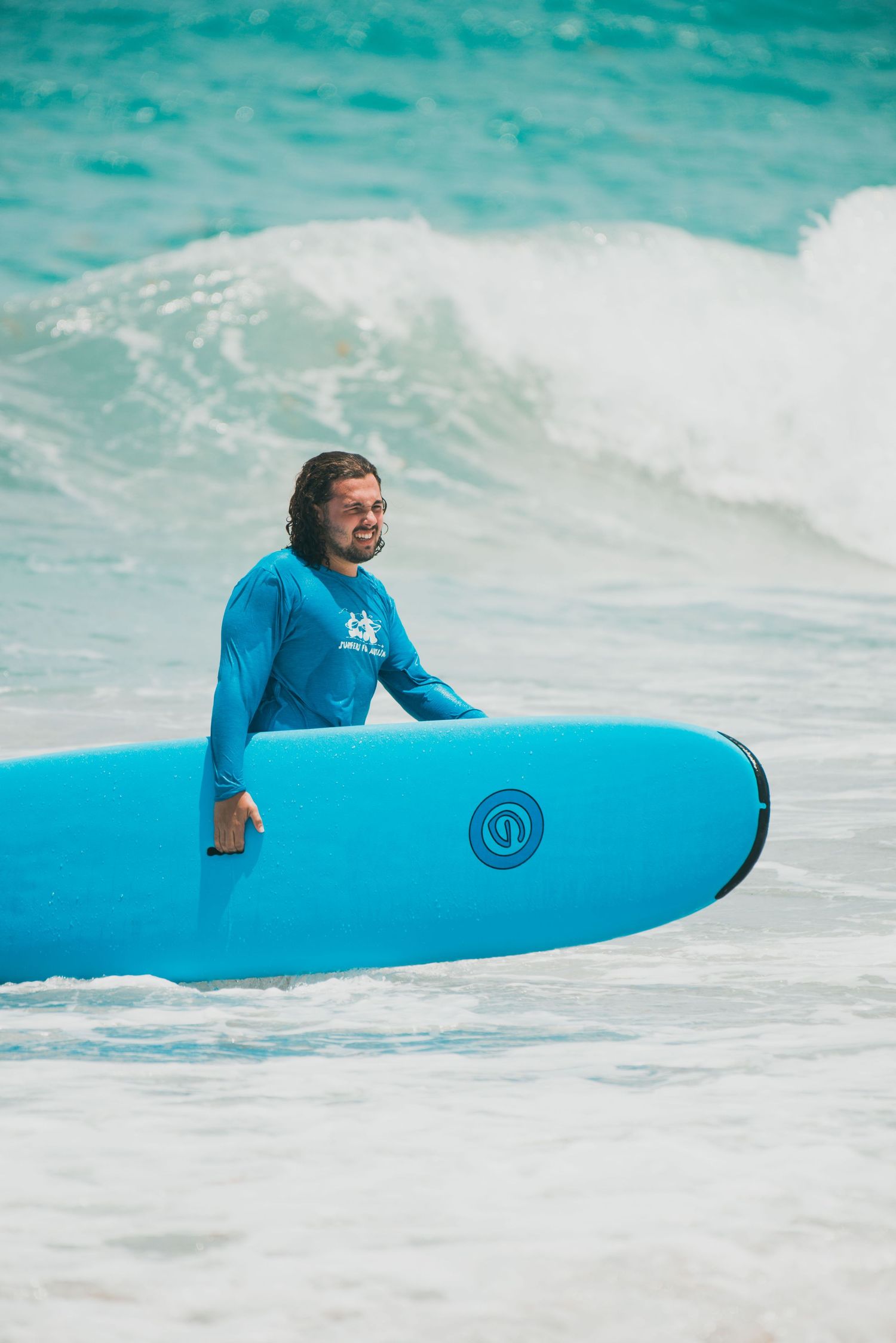 Instructor helps young child ride blue surfboard on ocean waves during surf lesson.