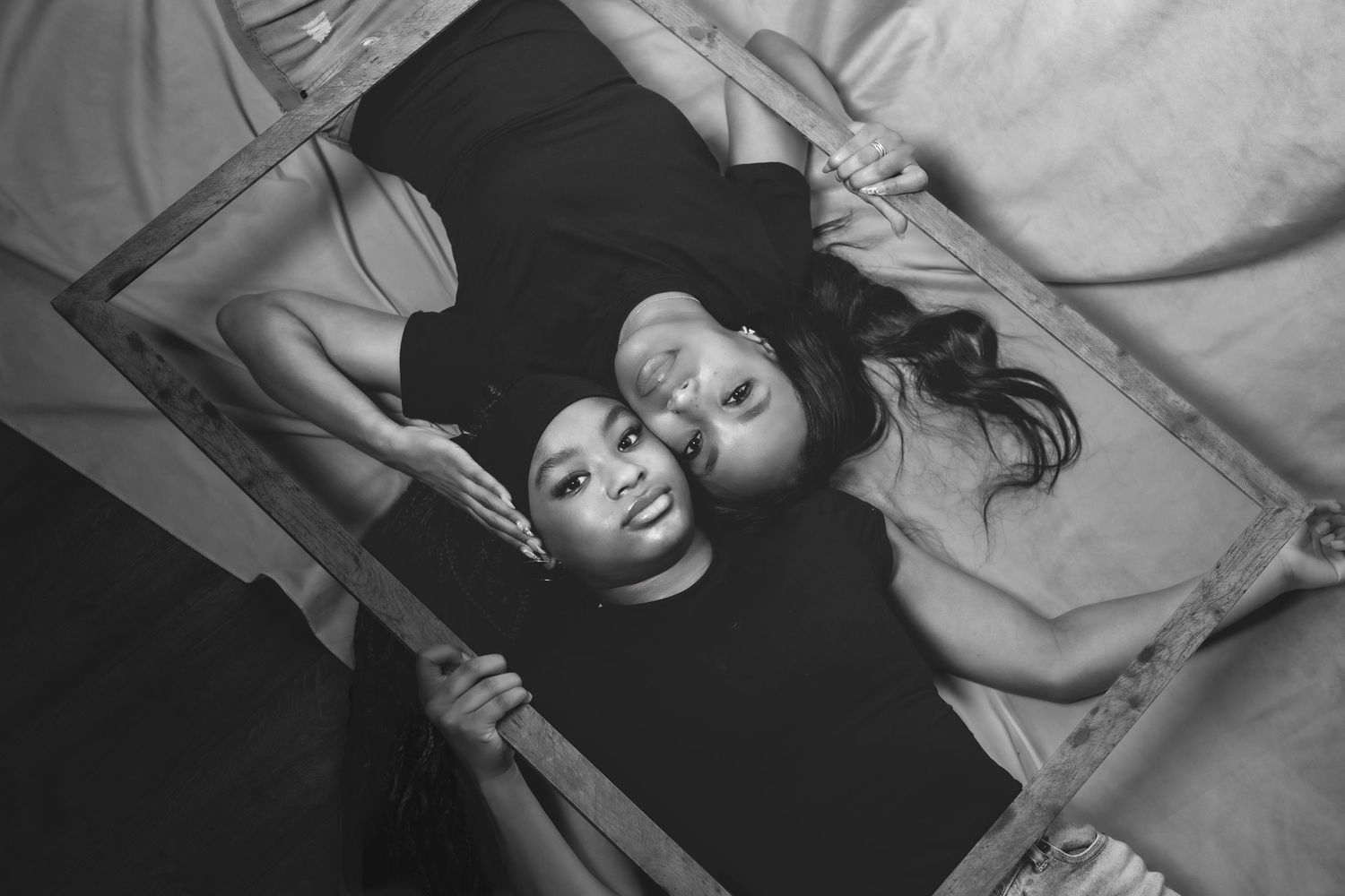 Mother and daughter lying down together inside a wooden frame, captured in a black and white overhead portrait photo.