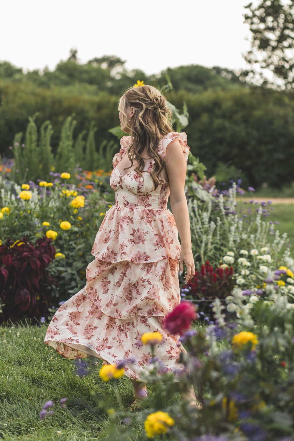 Woman in floral tiered dress walking through a colorful garden in bloom.