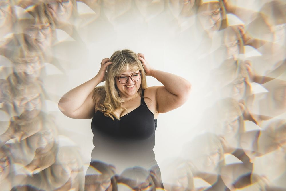 Smiling plus-size woman with glasses holds her head surrounded by a dreamy mirrored bokeh effect background.