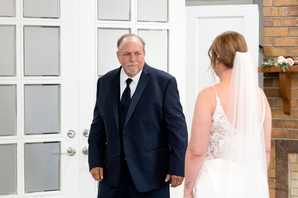 A bride in a white lace gown and veil shares a first look moment with a man in a navy suit and black tie.