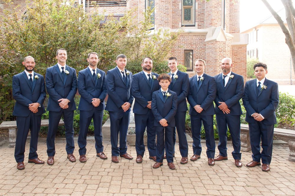 Groom and groomsmen posing in matching navy suits with boutonnieres outside a brick building.