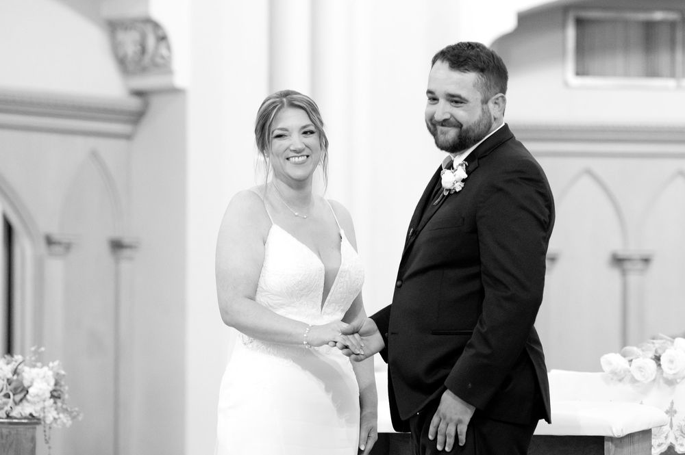 Smiling bride and groom holding hands at the altar during their church wedding ceremony in black and white.