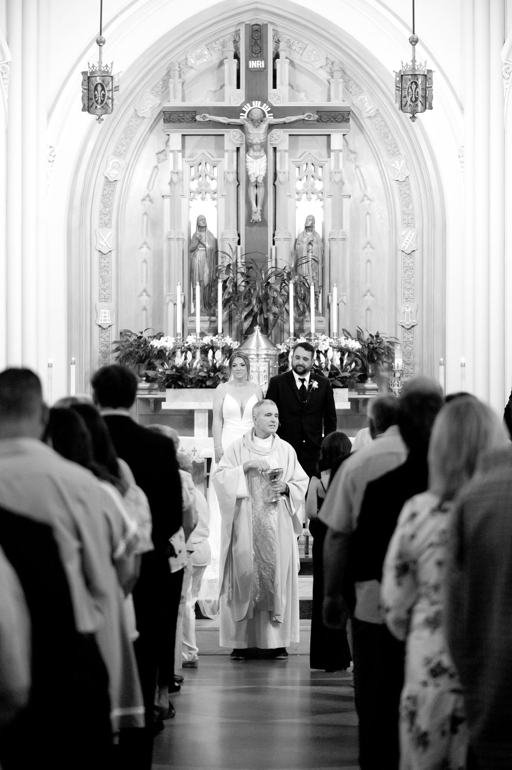 Black and white photo of a Catholic wedding ceremony with bride and groom at the altar, guests standing in pews.