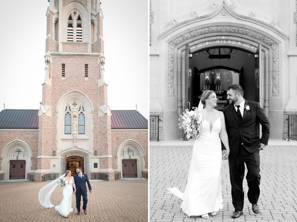 Bride and groom pose outside a brick church on their wedding day, with veil flowing in the wind.