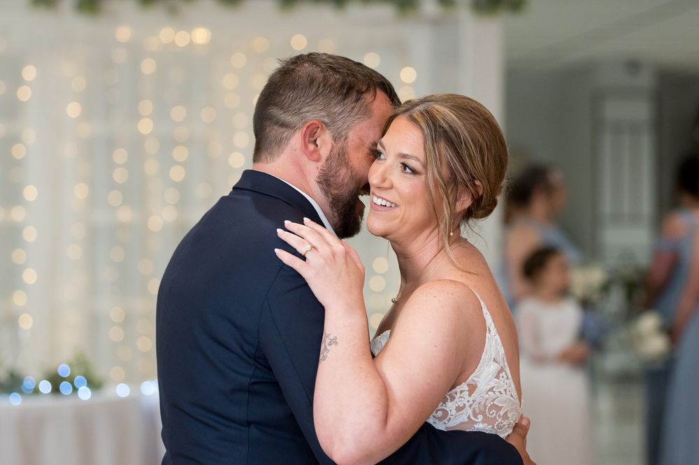 Bride and groom share a romantic first dance, smiling at each other in a softly lit reception venue.