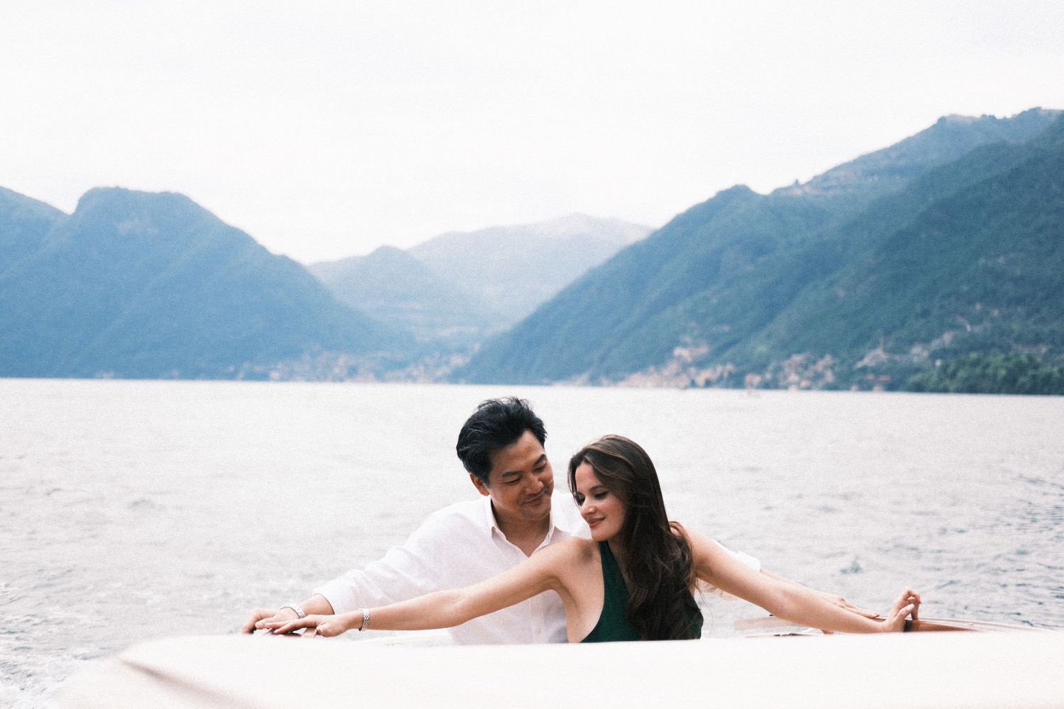 Couple smiling and leaning on a boat railing with scenic mountain lake views in the background.