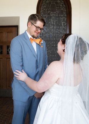 Bride in white gown and veil laughing with groom in blue suit and orange bow tie during wedding first look.