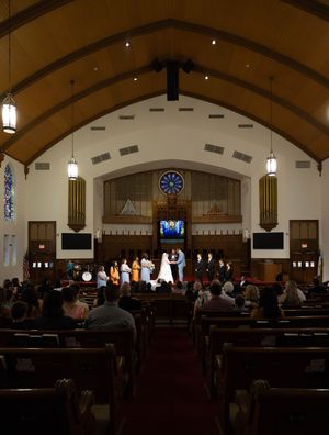 A wedding ceremony in a traditional church with vaulted ceilings, wooden pews filled with guests, and a couple at the altar.