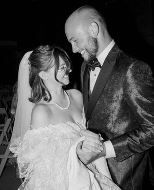 Black and white wedding photo of smiling bride in veil and groom in tuxedo gazing at each other.