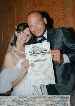 Newlywed couple smiling and holding their Texas marriage certificate, bride in white dress and veil, groom in dark suit.