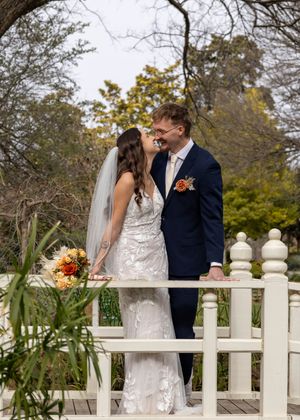 Bride and groom share a romantic moment on a white bridge surrounded by autumn trees in an outdoor garden wedding.