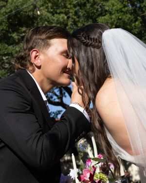 Bride and groom sharing their first kiss at outdoor wedding ceremony, bride in veil with braided updo holding colorful bouquet.