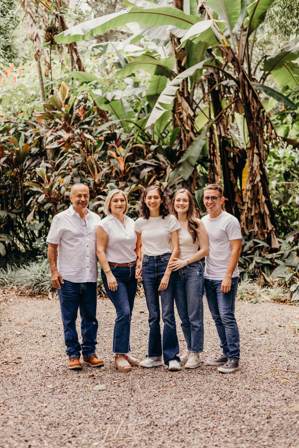 Five people in matching white shirts and jeans pose together against tropical garden backdrop.