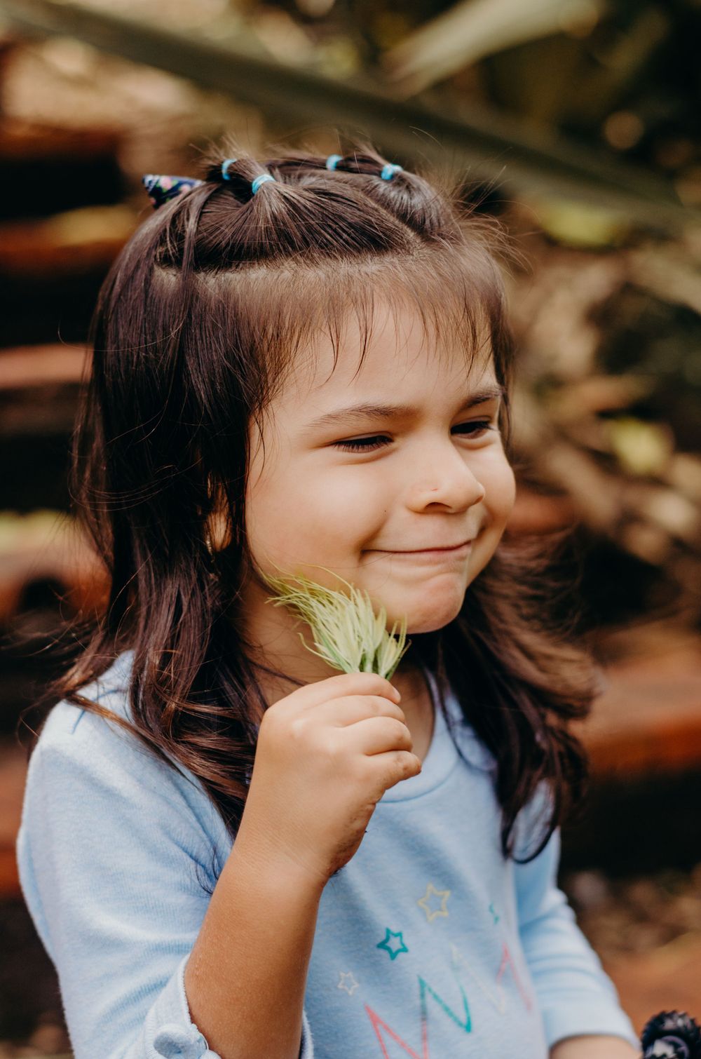 Young child smiling while holding a small flower against a blurred natural background.