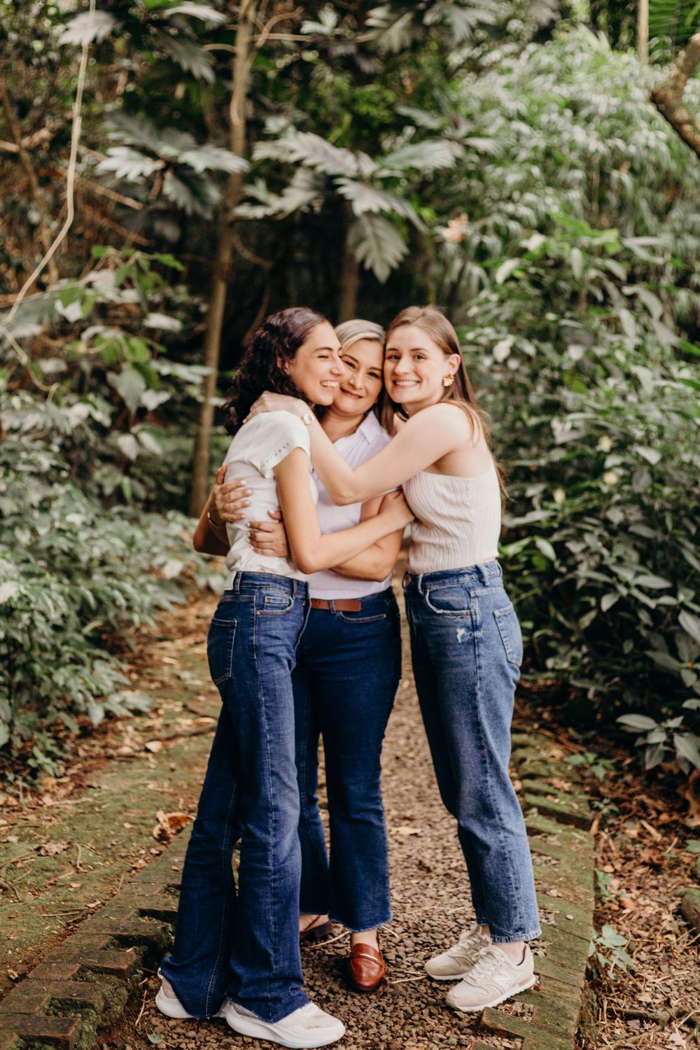 Three friends sharing an embrace on a forest path wearing matching casual outfits.