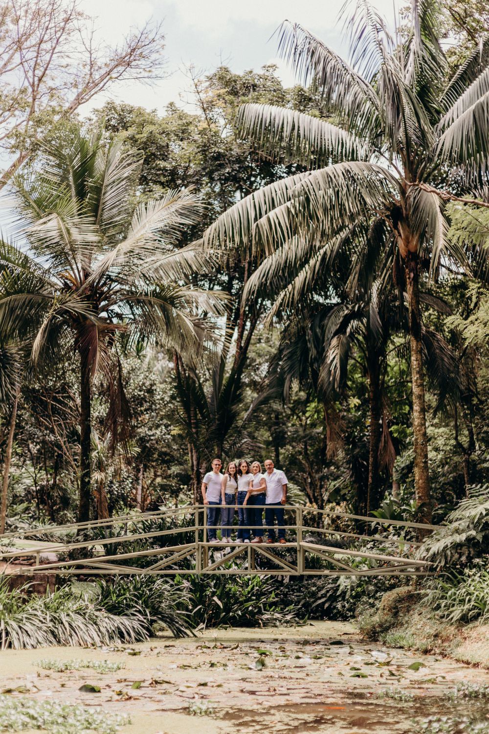Family photo on a wooden bridge surrounded by tropical palm trees and lush vegetation.