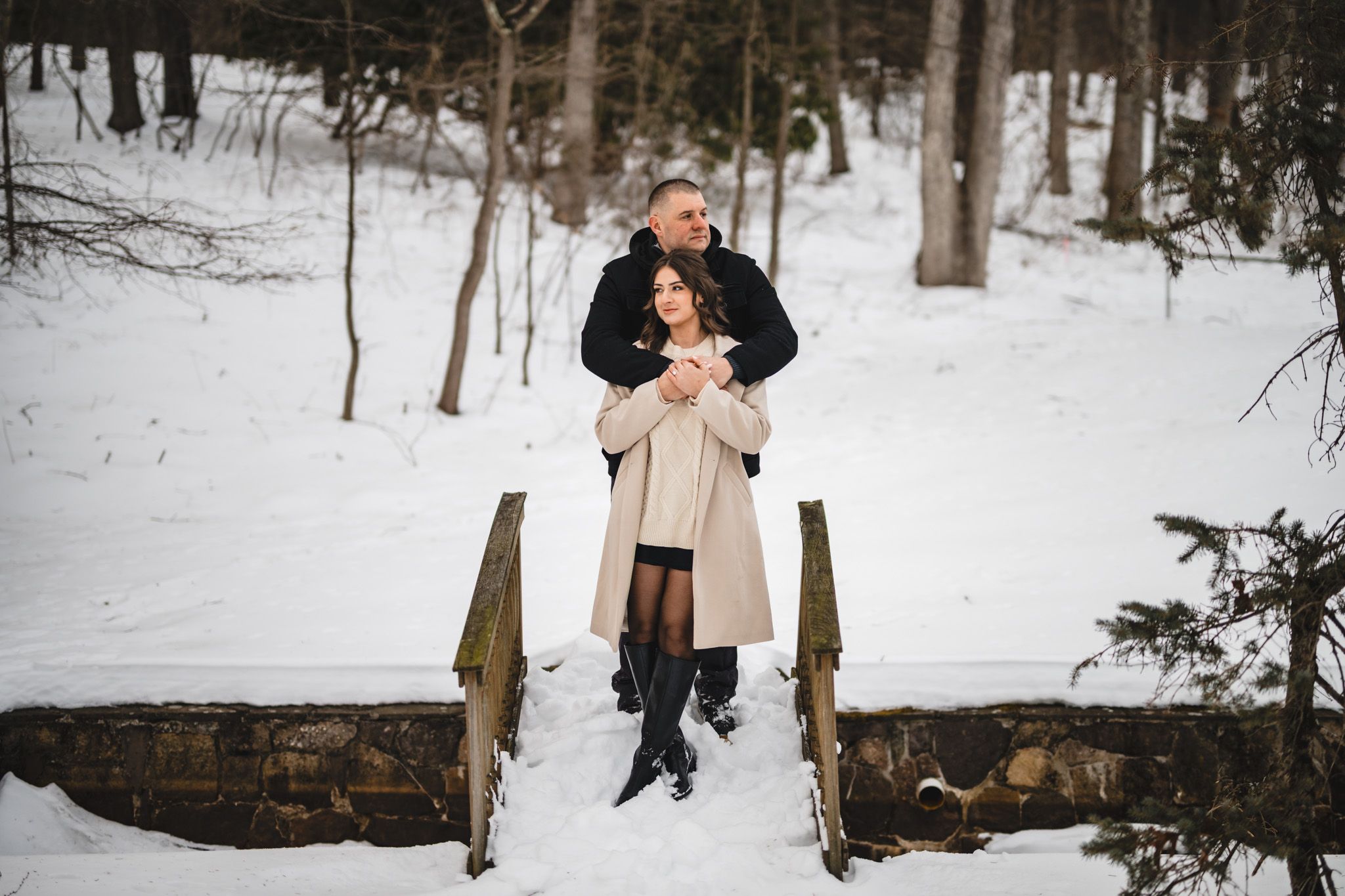 Romantic couple embracing on a snow-covered stone bridge in a winter forest.