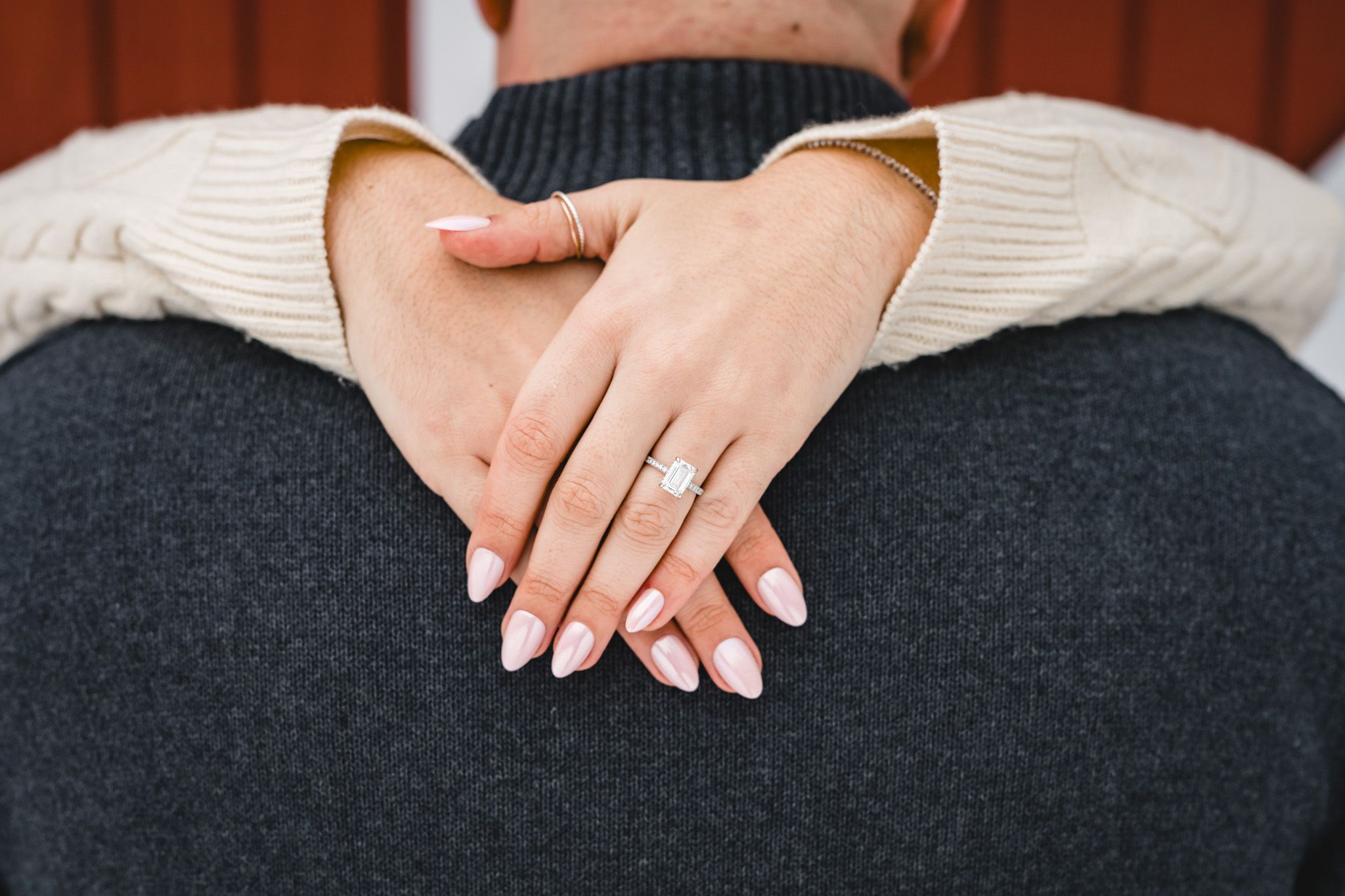 Close-up of a woman's hands with white manicure and diamond engagement ring resting on a man's gray sweater.