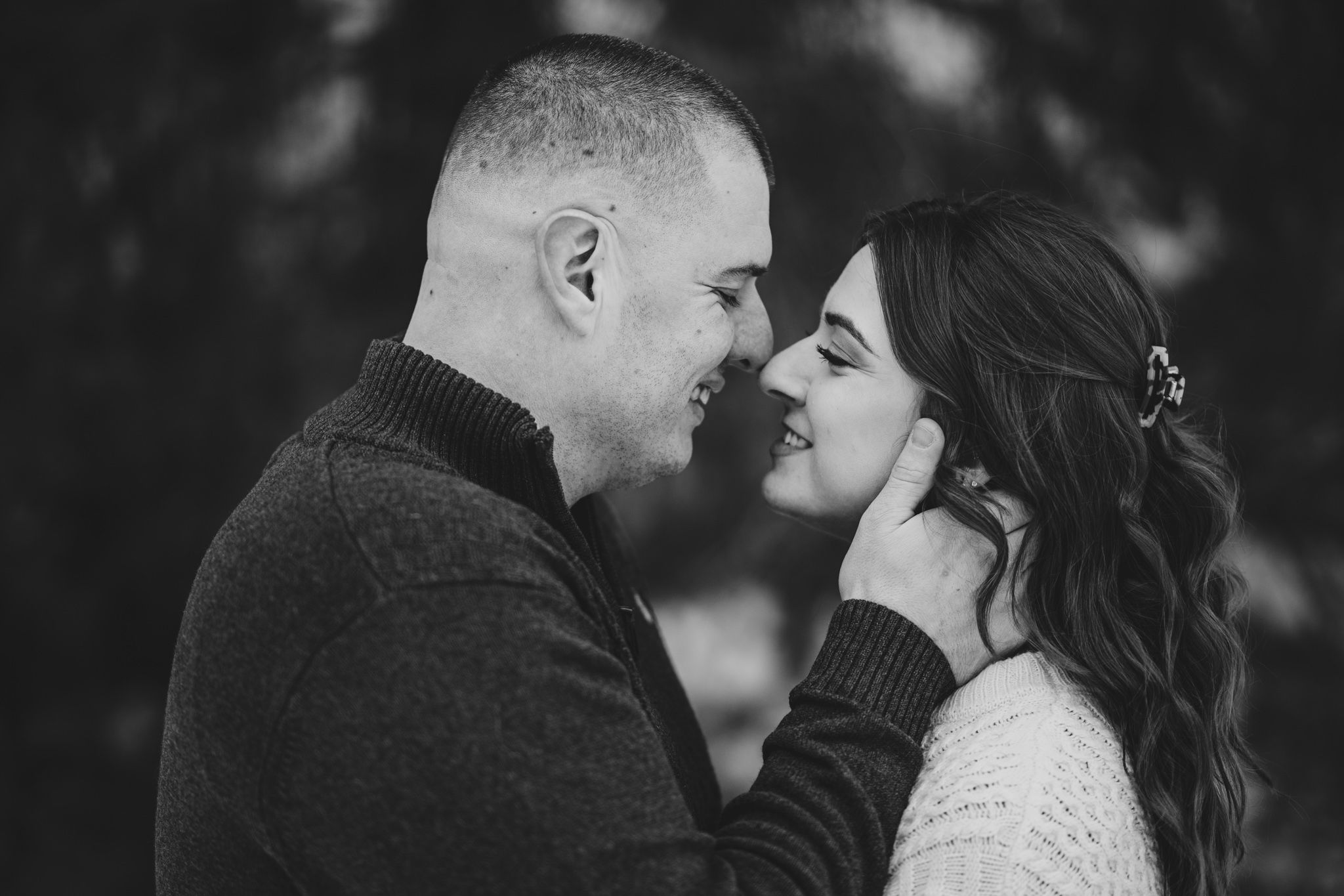 Black and white photo of a couple sharing a romantic moment, smiling and touching foreheads outdoors.