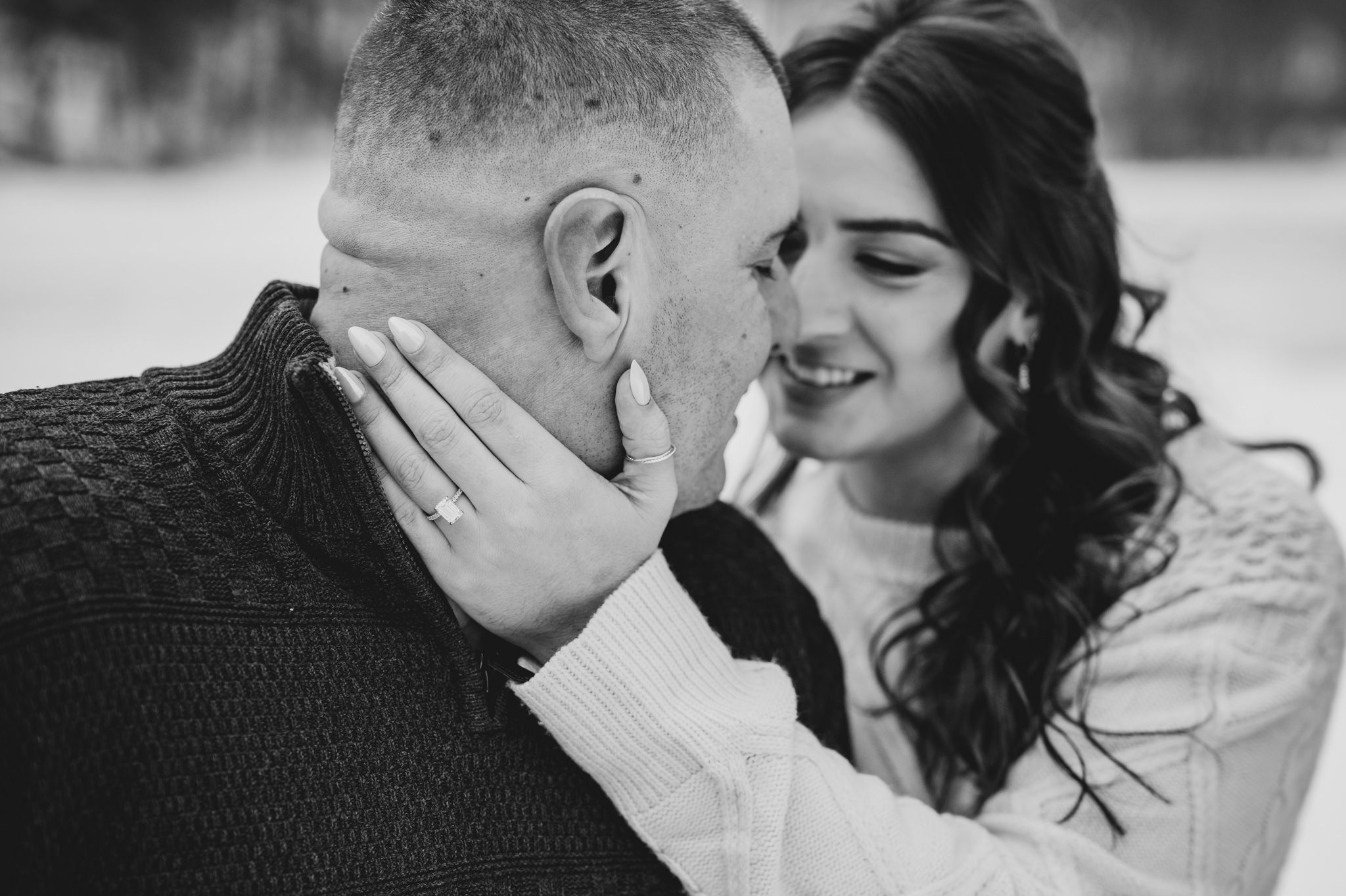 Black and white photo of a couple sharing a tender moment, woman smiling as she gently cups mans face outdoors.