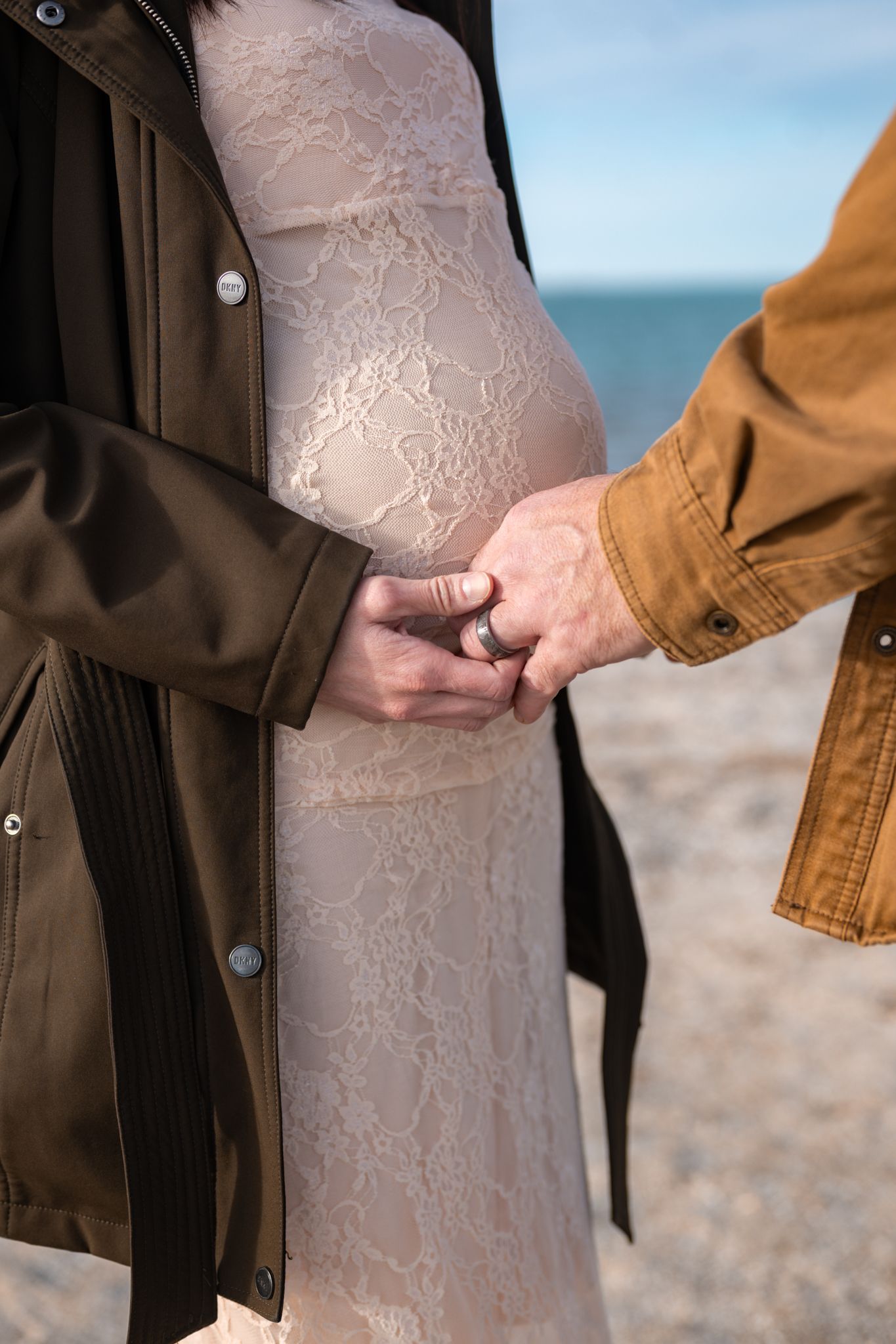 A couple holding hands in front of pregnant belly.