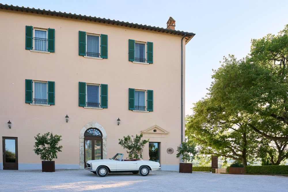 Elegant Italian villa with green shutters and a classic white convertible car parked in front.