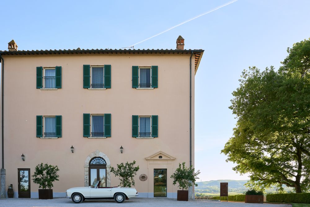 Charming Tuscan villa featuring green shutters, a white vintage convertible, and scenic countryside views.