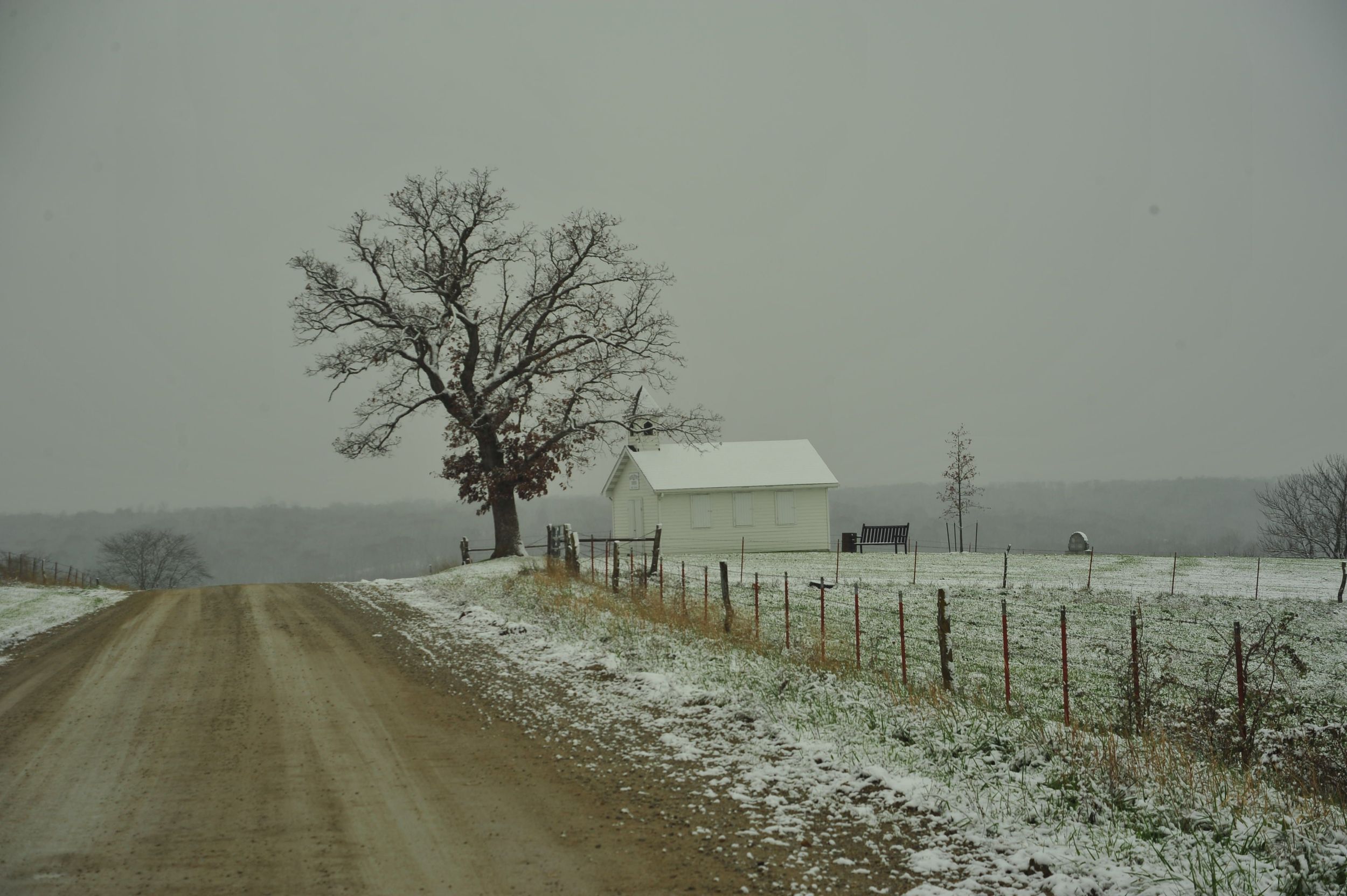 Snow dusted dirt road with white barn and bare oak tree in rural Northern Missouri winter