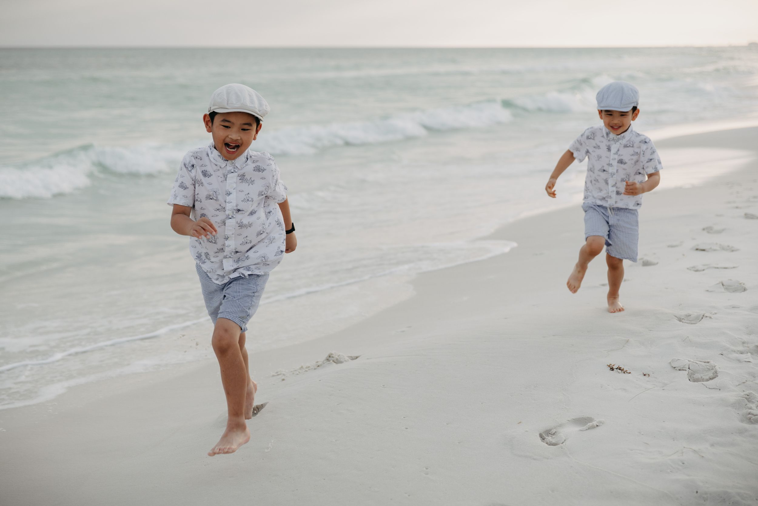 Couple holding hands walking along white sandy beach shoreline at sunset.