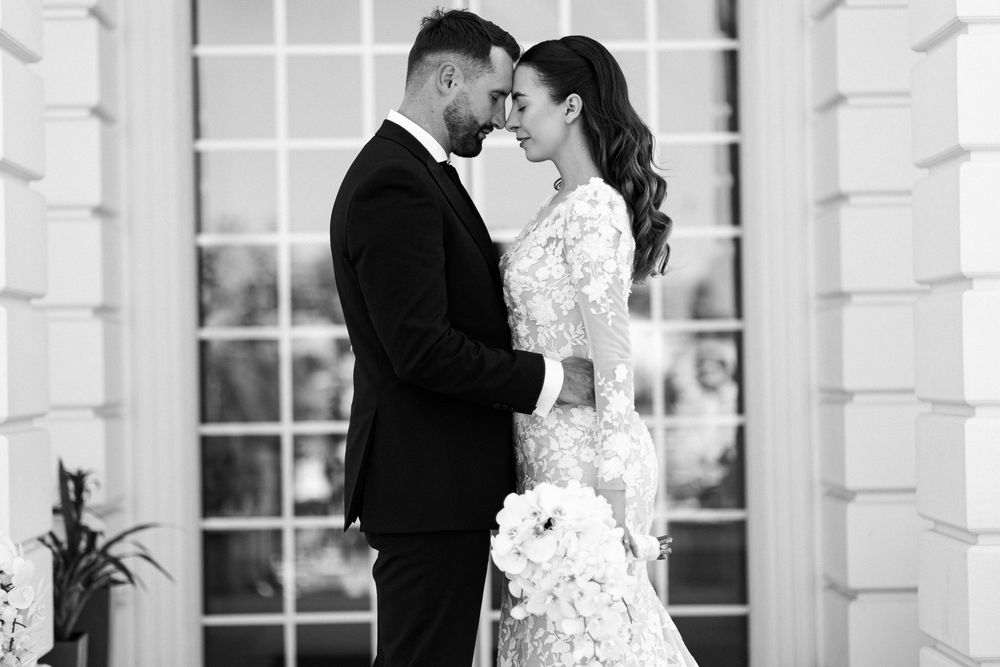 Elegant black and white wedding photo of bride and groom sharing an intimate moment outdoors.