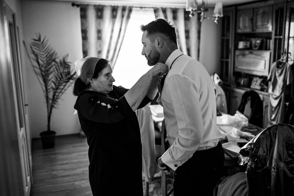 Black and white photo of woman adjusting grooms tie during wedding preparations indoors.