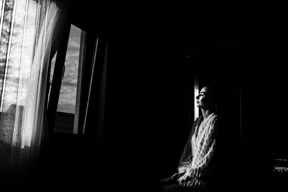 Black and white portrait of a bride sitting by a window in soft natural light.