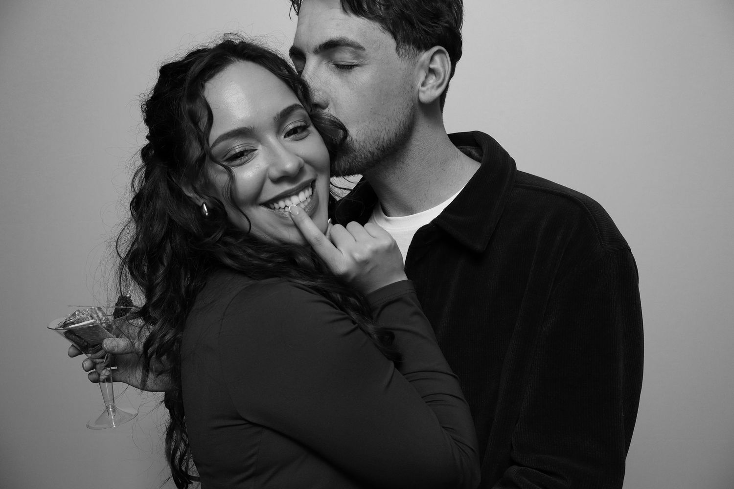 Black and white photo of a smiling woman and a man kissing her cheek in a romantic embrace.