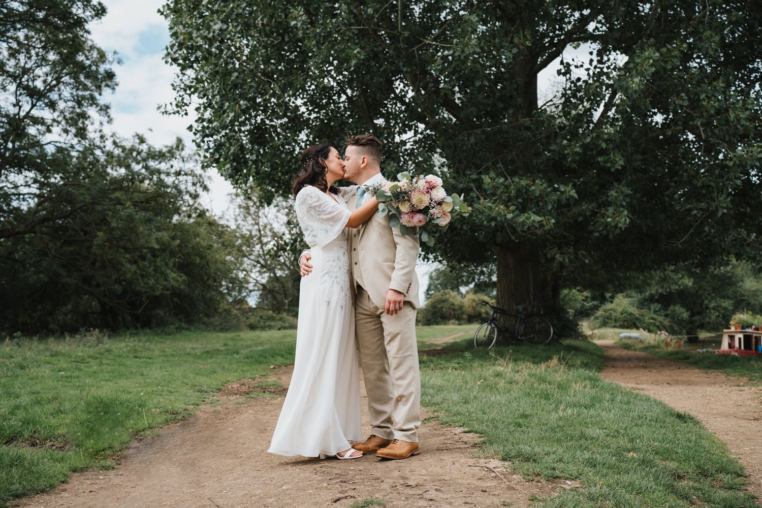 Bride and groom share a romantic kiss beneath a large oak tree in countryside setting at Oxford Port Meadow with The Perch Pinsey Wedding Ve