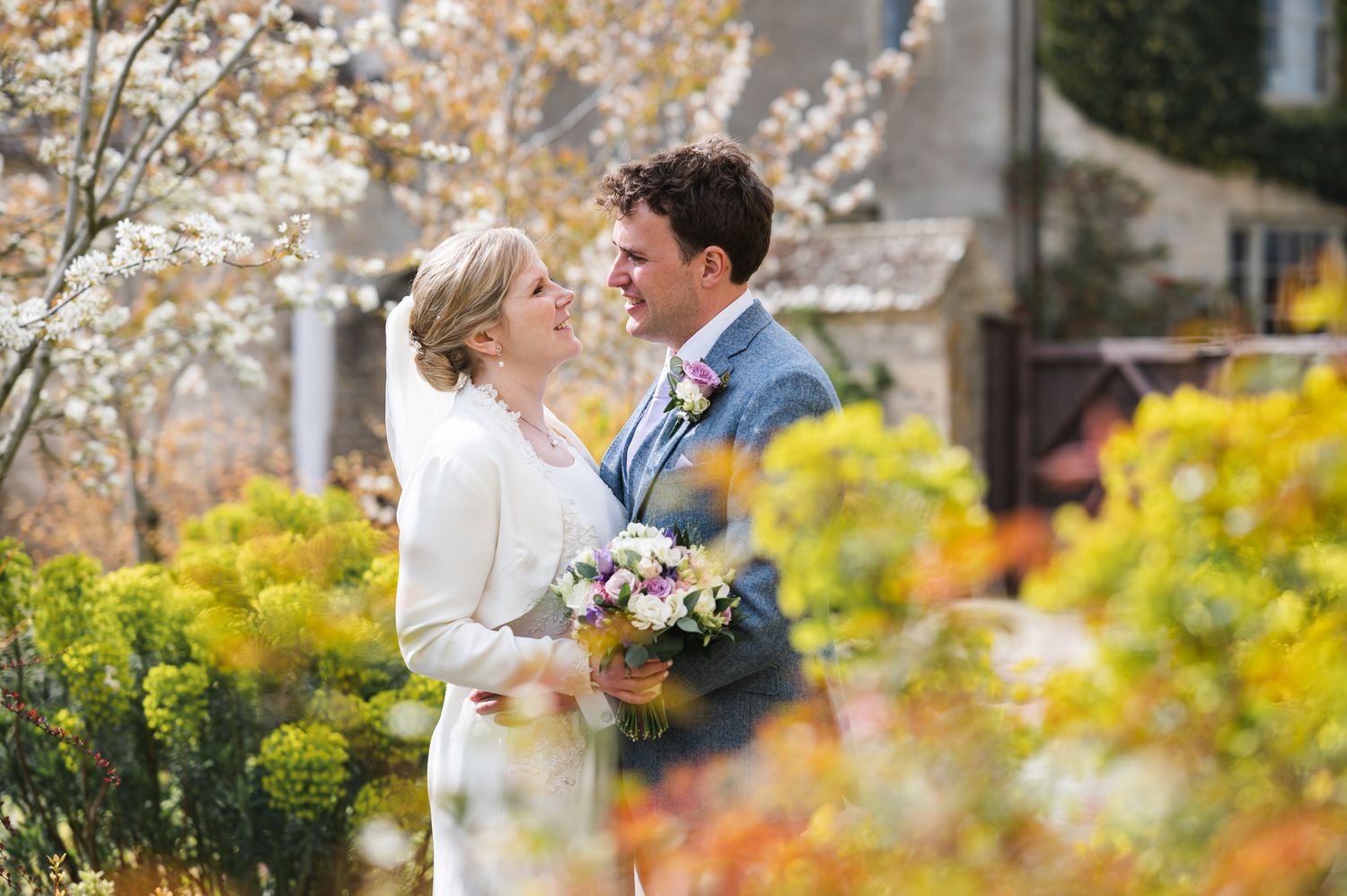 Smiling bride and groom embracing among colourful spring garden blooms on their wedding day at Caswell House