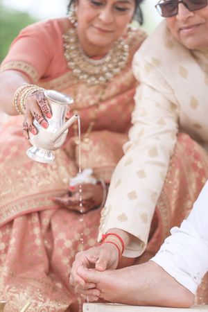 Indian wedding ritual with woman pouring water from silver vessel over joined hands during traditional Hindu ceremony.