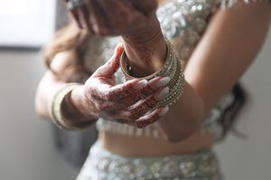 Close-up of Indian bride's hands adorned with intricate henna mehndi and gold bangles in traditional bridal jewelry.