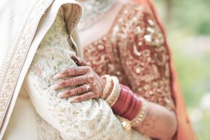 Indian bride with intricate henna hands holding groom in traditional embroidered wedding attire with gold bangles.